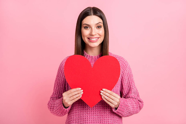 Portret van brunette optimistisch meisje houden hart dragen roze trui geïsoleerd op karmozijn kleur achtergrond. - Foto, afbeelding