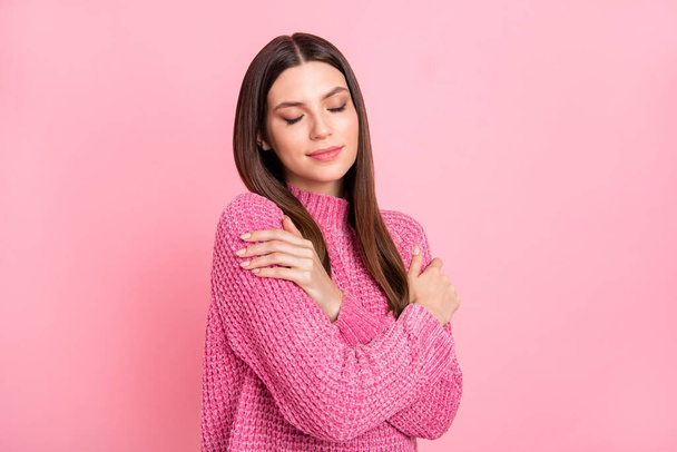 Portrait of brunette optimistic girl hug herself wear pink sweater isolated on crimson color background. - Photo, image