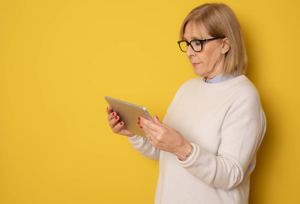 Senior woman using tablet isolated on yellow background - Fotoğraf, Görsel