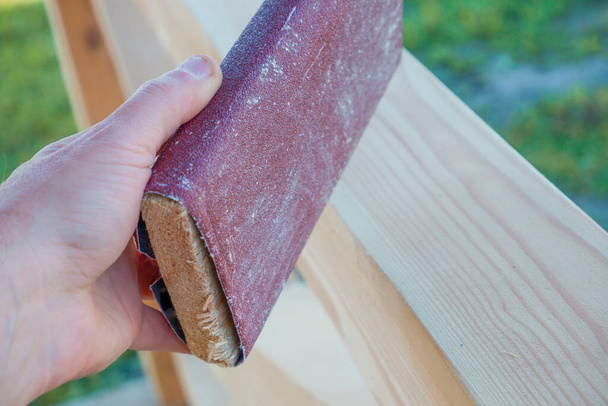 Lijando madera. Un carpintero macho está lijando las vigas de madera de un mirador hecho. Mano de un carpintero frotando madera con papel de arena - Foto, Imagen