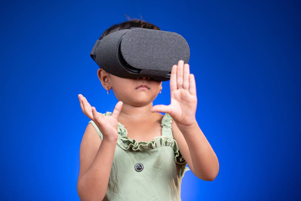 Litle girl kid enjoying VR or virtual goggles by feeling on blue background - έννοια των παιδιών που χρησιμοποιούν σύγχρονη τεχνολογία Entertainment και γενιά Z έννοια - Φωτογραφία, εικόνα
