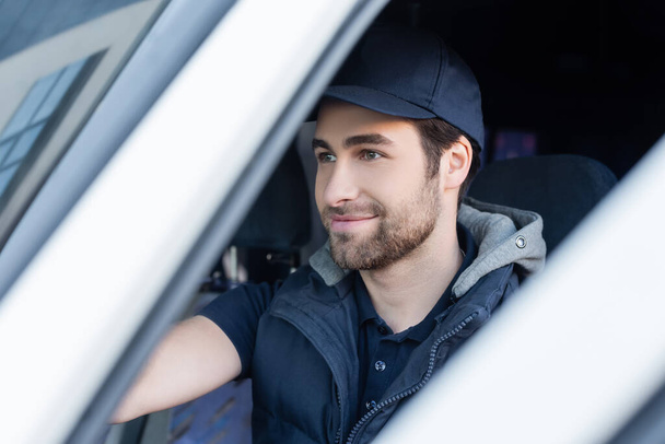 Smiling courier in uniform sitting in blurred car  - Фото, изображение