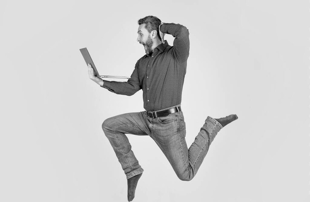 удивленный энергичный человек прыгает во время работы в Интернете на ноутбуке спешите за покупками, сюрприз. - Фото, изображение