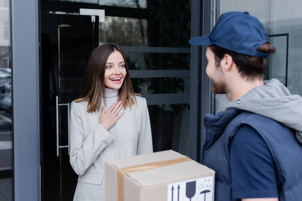 Excited woman looking at blurred courier near door of building outdoors  - Photo, image