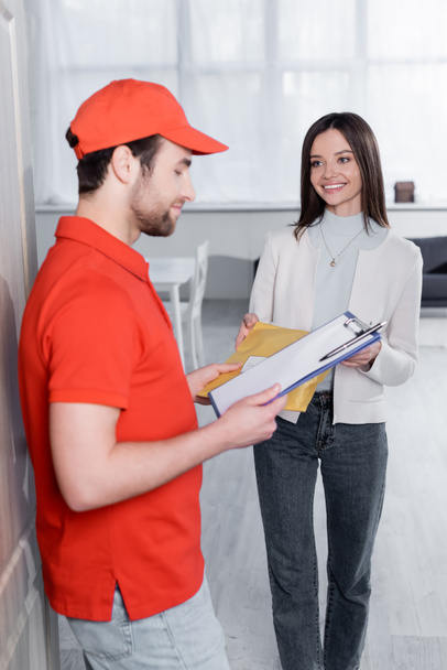 Positive woman taking parcel from delivery man with clipboard in hallway  - Foto, Imagem