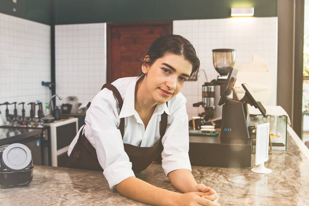 Bela barista feminina em pé na frente do balcão de barista sorrindo, ela está pronta para fazer café delicioso, servindo clientes e qualidade, ela olha para você encantador. - Foto, Imagem