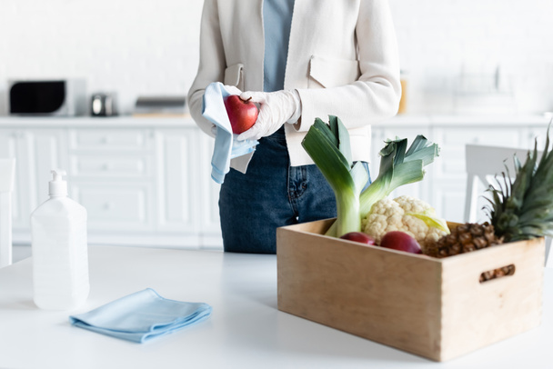 Cropped view of woman in latex gloves cleaning apple with rag at home  - Photo, image