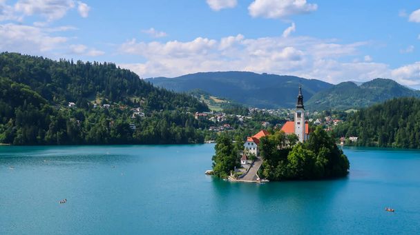 Veduta della chiesa cattolica situata su un'isola sul lago di Bled con montagne e villaggi sullo sfondo nelle Alpi slovene - Foto, immagini