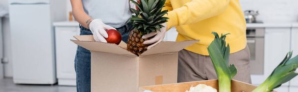 Cropped view of couple in latex gloves taking fruits from box in kitchen, banner  - Photo, image