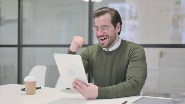 Jeune homme d'affaires célébrant le succès sur tablette au bureau - Photo, image