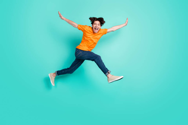 Full size photo of cool brown hair young guy jump yell wear t-shirt jeans sneakers isolated on blue background. - Fotoğraf, Görsel