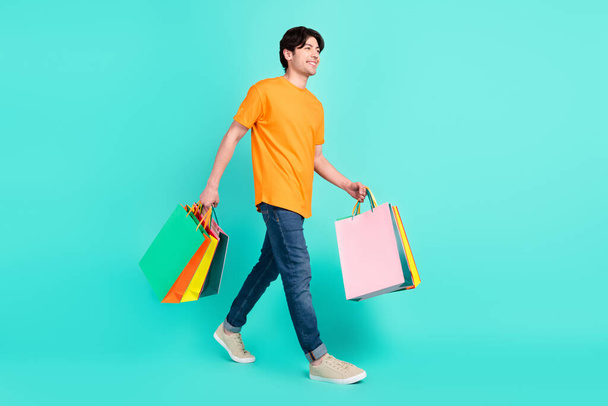 Full size profile photo of nice brown hair millennial guy go with bags wear t-shirt jeans sneakers isolated on blue background. - Zdjęcie, obraz