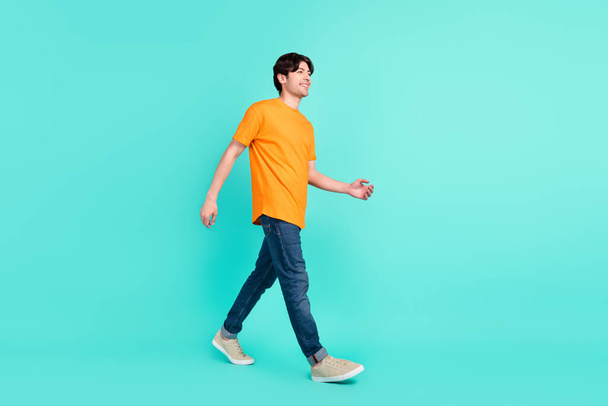Full length profile photo of good brown hair millennial guy go wear t-shirt jeans sneakers isolated on blue background. - Foto, imagen