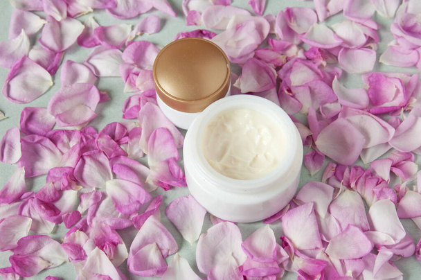 Crème cosmetische in fles, verse roze roos bloemen en bloemblaadjes, natuurlijke cosmetische, close-up - Foto, afbeelding