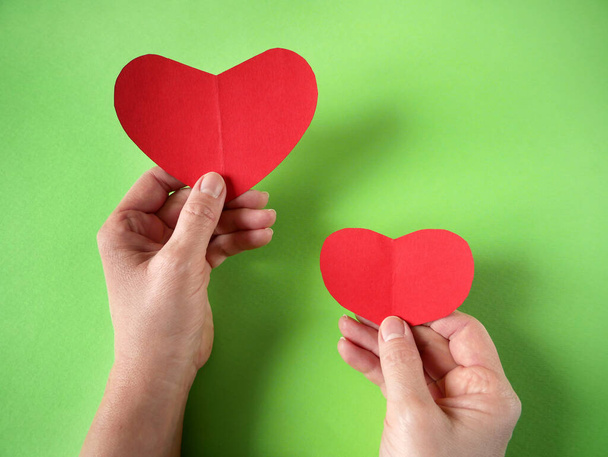 El ele tutuşan iki kırmızı kalp. Aşk ve Sevgililer Günü 'nün sevgili kavramı. Aile sigortası konsepti. Dünya kalp günü. Aşk konsepti. Üst görünüm - Fotoğraf, Görsel