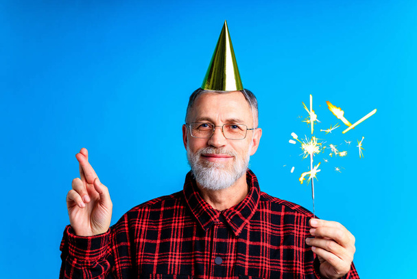 man wearing birthday hat with sparkler isolated on bright blue colour background, studio portrait - Foto, afbeelding