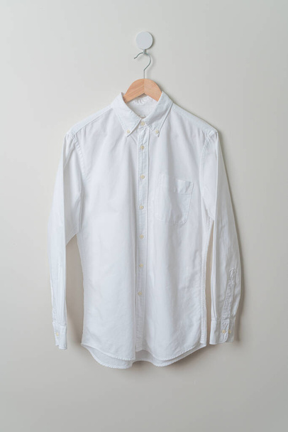 hanging white shirt with wood hanger on wall - Foto, Bild