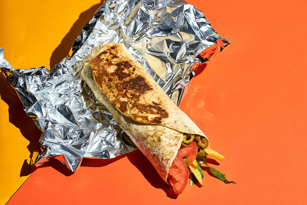 Shawarma roll in foil on a bright orange background - Fotografie, Obrázek