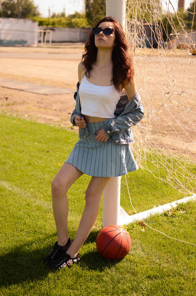 A young girl stands on the football field. A brunette girl with long hair stands sits on a soccer field with a ball. - 写真・画像