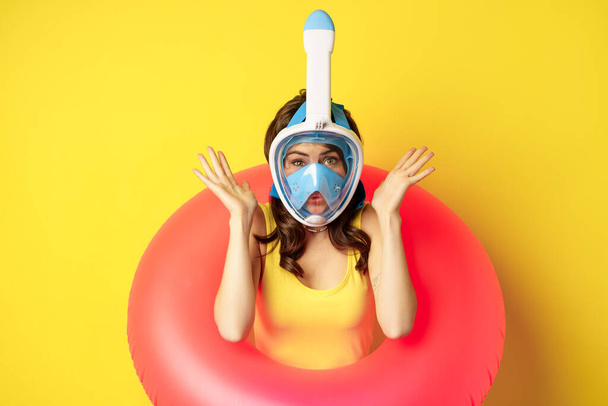 Портрет молодой женщины в отпуске в маске для подводного плавания и купания, стоящей на жёлтом фоне - Фото, изображение