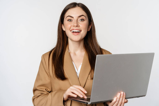 Portrait of corporate woman working with laptop, smiling and looking assertive, white background - Photo, Image