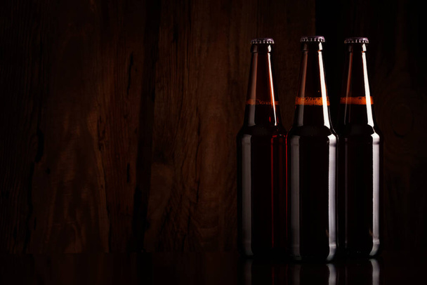 Three brown glass beer bottles on a wooden wall background - 写真・画像