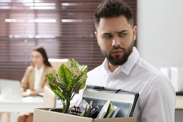Upset dismissed man carrying box with personal stuff in office - Foto, Imagen