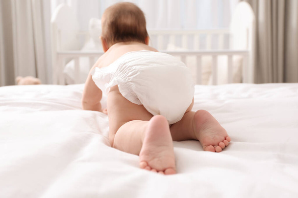 Little baby in diaper on bed at home, back view - Foto, Imagen