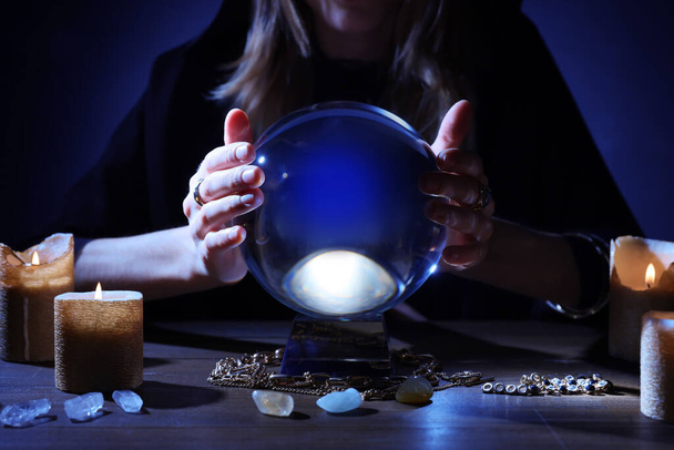 Soothsayer using crystal ball to predict future at table in darkness, closeup. Fortune telling - Foto, Imagem