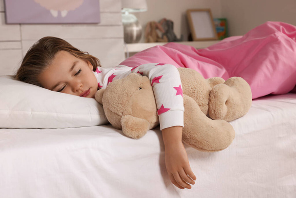 Cute little girl with toy bear sleeping in bed at home - 写真・画像