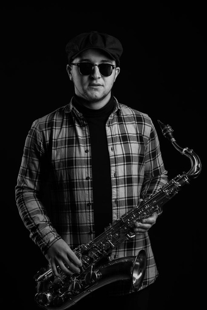 Brutal Sexy Sax Player is Holding a Saxophone. Jazz Saxophonist has Tenor Sax. Black and White. Black Background. Close-up - Zdjęcie, obraz