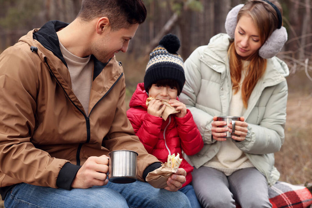 Happy family with sandwiches and hot drinks spending time together in forest - Foto, Bild