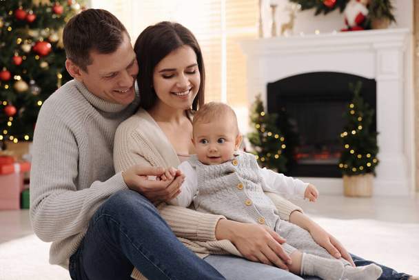 クリスマスのために飾られた部屋で床の上にかわいい赤ちゃんを持つ幸せな家族 - 写真・画像