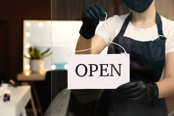 Woman hanging Open sign onto glass door in salon, closeup. Beauty services during Coronavirus quarantine - Fotografie, Obrázek