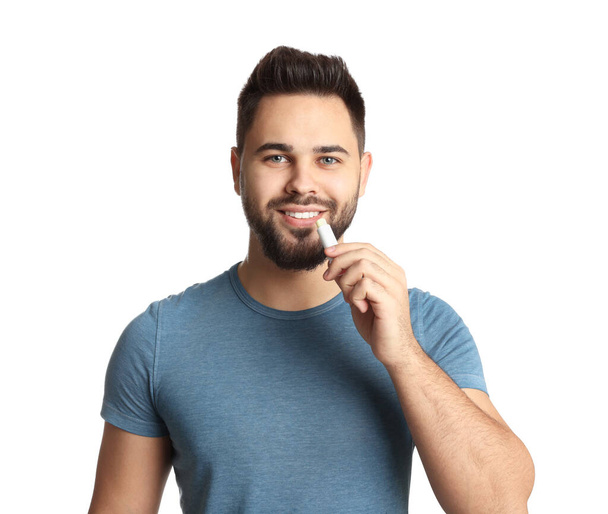 Young man applying lip balm on white background - Fotó, kép