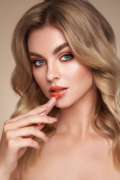 A beautiful young blonde woman applying lipstick. Model with healthy skin, close up portrait. Cosmetology, beauty and spa - Foto, Imagen