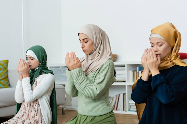 Interracial women in hijabs praying near child at home  - Foto, Bild