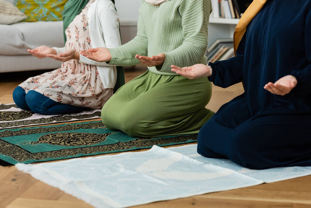 Vista recortada de mujeres musulmanas con ropa tradicional rezando sobre alfombras en casa  - Foto, imagen