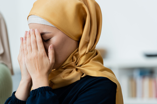 Asian woman in hijab covering face while praying at home  - Valokuva, kuva