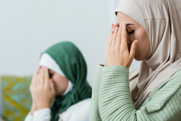 Arabian woman covering face while praying near daughter at home  - Foto, Imagem