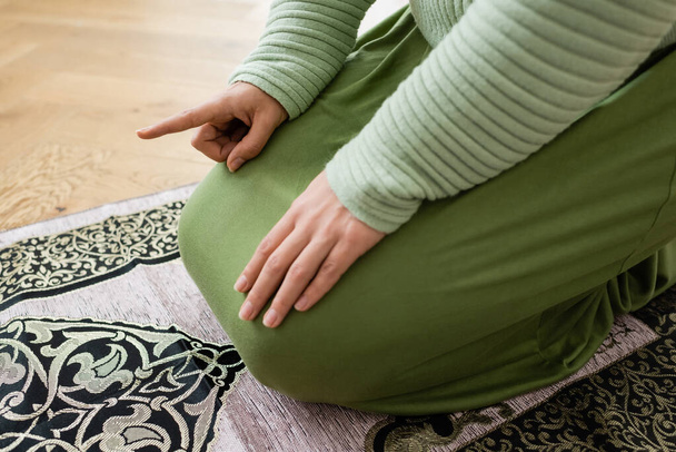 Oříznutý pohled na arabskou ženu ukazující prstem při modlitbě na koberec doma  - Fotografie, Obrázek