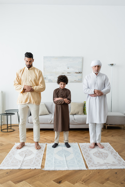 Többnemzetiségű férfiak és arab fiú otthon a szőnyegen imádkoznak  - Fotó, kép