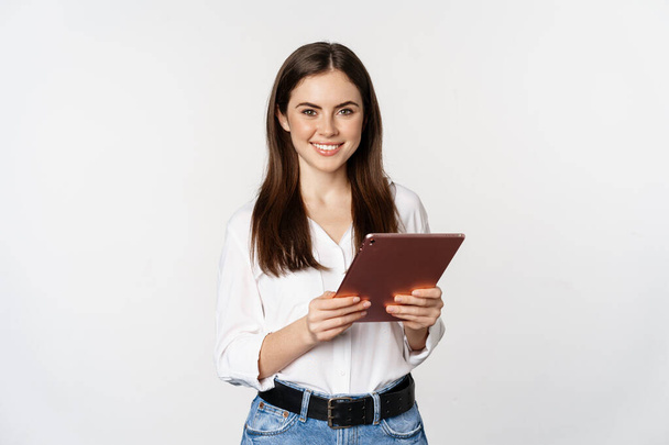 Portrait of smiling corporate woman looking at digital tablet, working, standing over white background - Foto, immagini