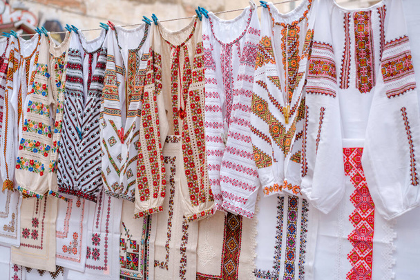 La ropa diferente ucraniana de la vendimia - las camisas tradicionales bordadas, vyshyvanka. Tradicionales vestidos ucranianos en el mercado de pulgas Vernissage en Lviv, concepto de compras de ahorro. Enfoque selectivo - Foto, imagen