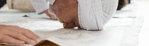 Widok z boku dojrzały mężczyzna modlący się na dywanie w domu, sztandar  - Zdjęcie, obraz