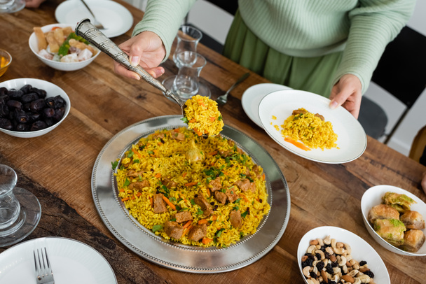 Cropped view of muslim woman serving pilaf near tasty food on table  - Фото, изображение