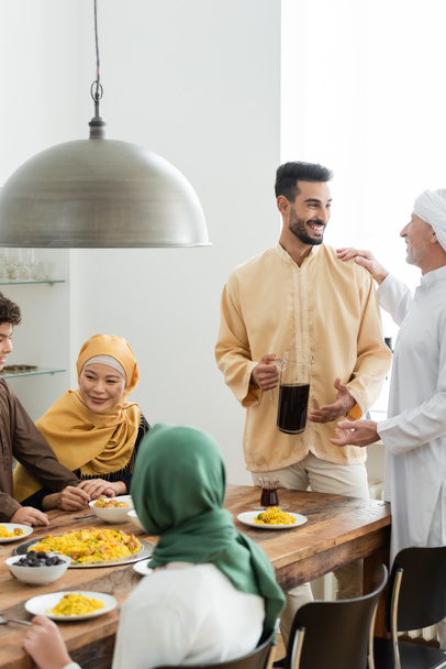 maduro hombre hablando con araban hijo cerca interracial musulmán familia y comida en casa  - Foto, Imagen