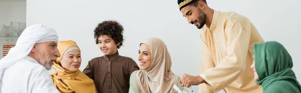multiethnische muslimische Familie lächelt neben arabischem Mann mit Krug zu Hause, Banner - Foto, Bild