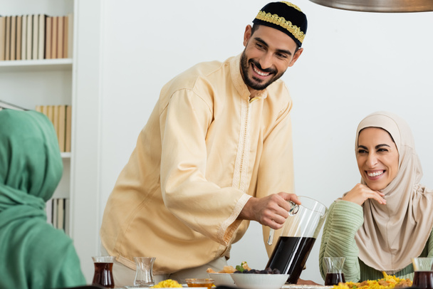 felice uomo musulmano in skullcap versando tè vicino donna felice in hijab - Foto, immagini