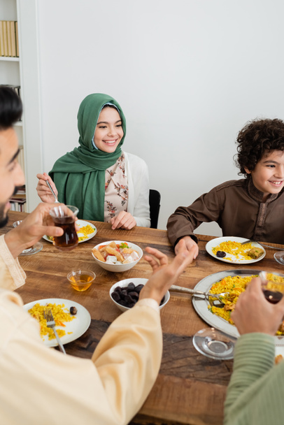 happy interracial muslim kids having dinner with blurred parents at home - Foto, Imagem